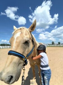 Young girl with riding helmet hugging a horse