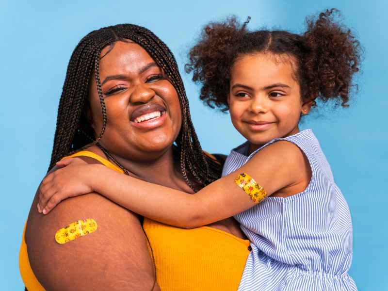 A mom holding her daughter, each with a colorful Band-Aid on their arm, representing they received the flu shot