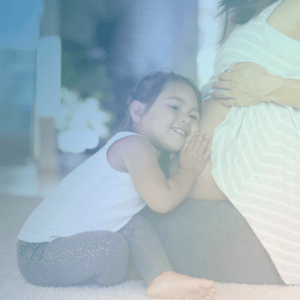 Image of a pregnant individual with her toddler's head on her belly, listening.